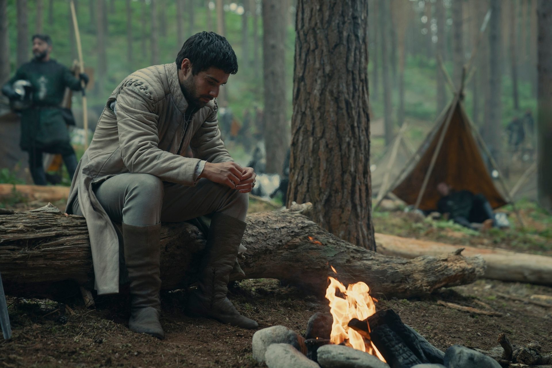 Fabien Frankel as Criston Cole in House of the Dragon season 2 sitting by a fire on a large log