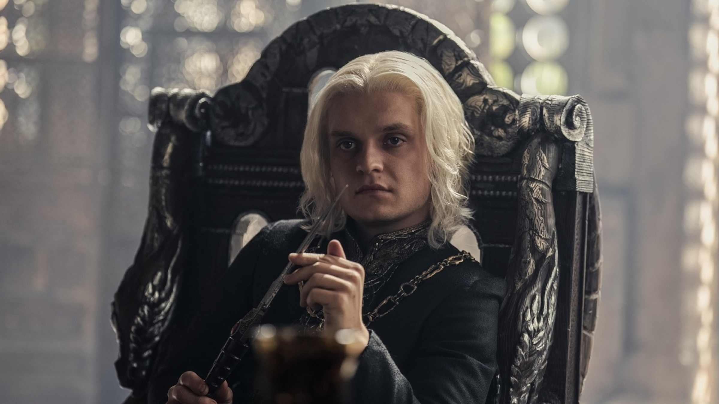 Aegon Targaryen sitting at a table and holding a knife in House of the Dragon